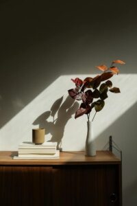 Books on a wooden sideboard next to a white slender ceramic vase with pink hued flowers