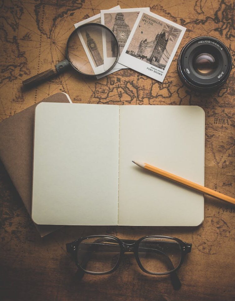 How I find and select makers and artisan businesses for opportunities that promote and showcase their craftwork Vintage style image of a notebook, yellow pencil, old sepia photographs under a magnifying glass, black framed eyeglasses and a camera lens on a wooden desk